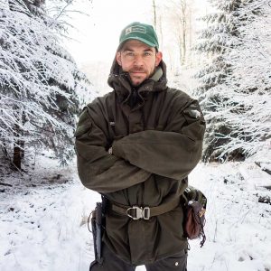 Maurice Ressel Inhaber der Wildnisschule Lupus schaut in einer Schneelandschaft in die Kamera und lacht