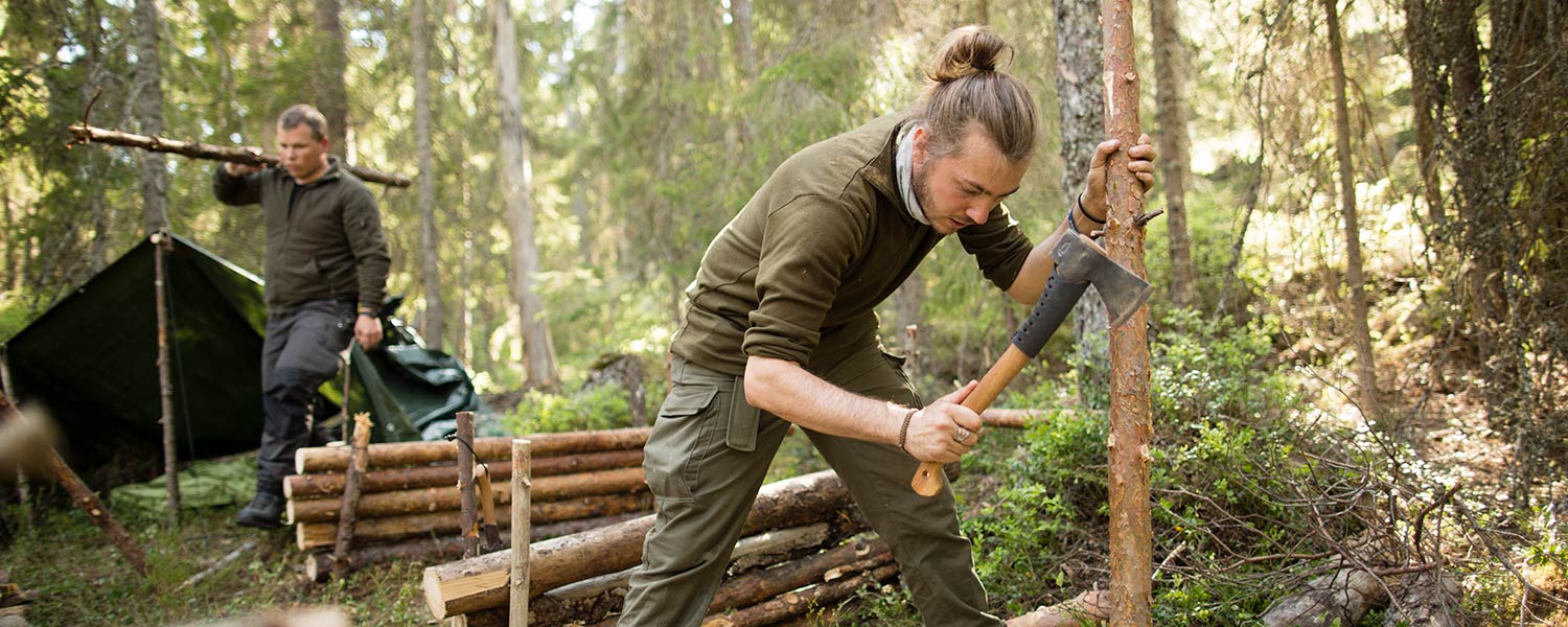 teambuilding-berlin-survival Zwei Männer bauen in einem Schwedischen Wald ein Notlager aus Holz und Plastikplanen.