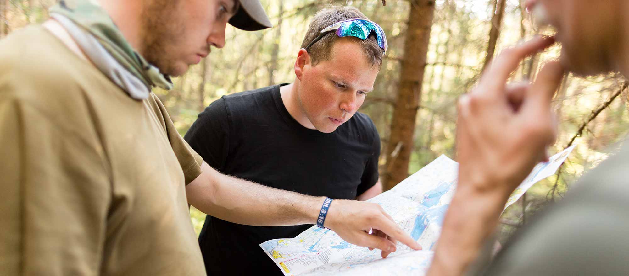 Teambuilding Maßnahmen der Wildnisschule Lupus bei Berlin Drei Teilnehmer eines Teambuilding Kurses bei Berlin beugen sich über eine Karte zu Navigation.