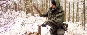 Der Survival Trainer Maurice Ressel hackt mit seinem Messer Feuerholz. Er kniet dabei in einer Landschaft voller Schnee.