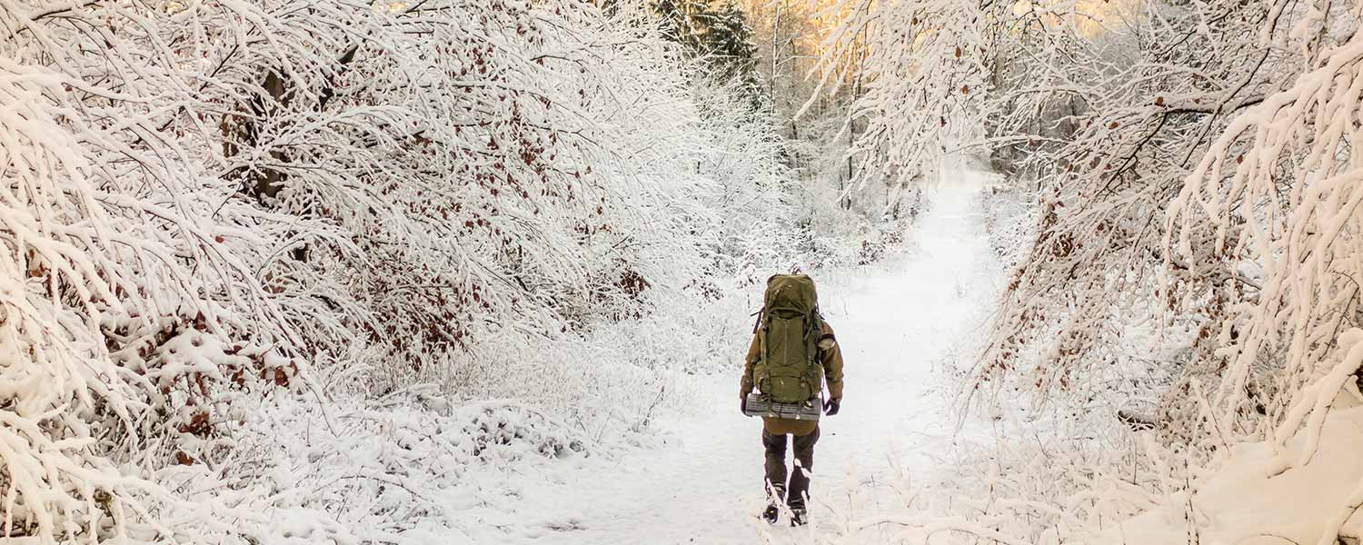 Ein Teilnehmer unserer Survivals Trainings läuft mit seinem Rucksack durch eine verschneite Landschaft.