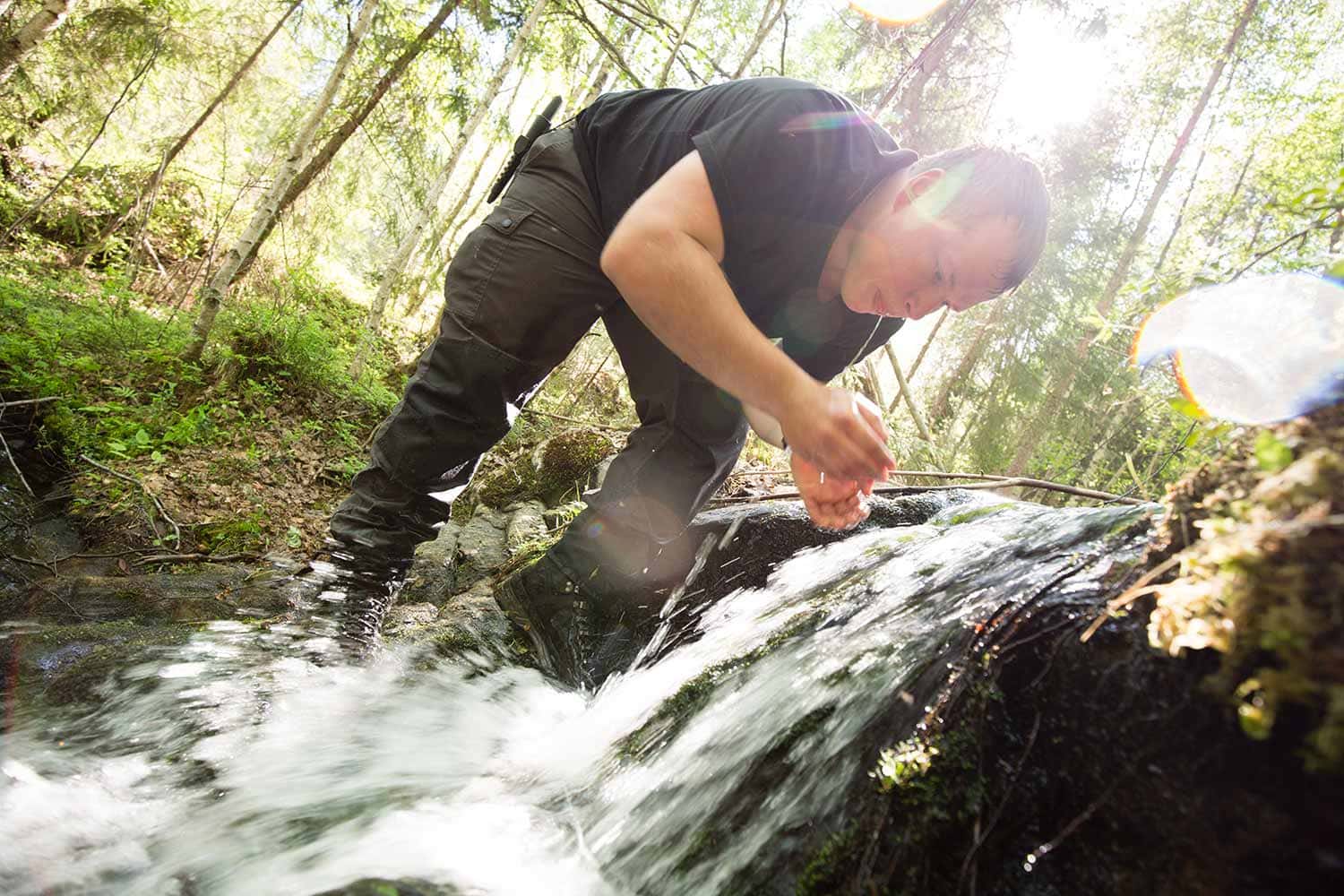 Ein Teilnehmer des Wildnispädagogik-Studiums schöpft mit seiner Hand Wasser aus einem kleinen Wasserfall der mitten im Wald liegt.