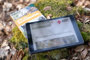 Ein I-Pad und ein Erste-Hilfe Handbuch liegen auf dem Waldboden. Nach unserem Erste-Hilfe-Kurs ist jeder Teilnehmer selber verantwortlich für seine Weiterbildung. Mit dem kostenlosen Download von nützlichen PDF unterstützen wir sie dabei.