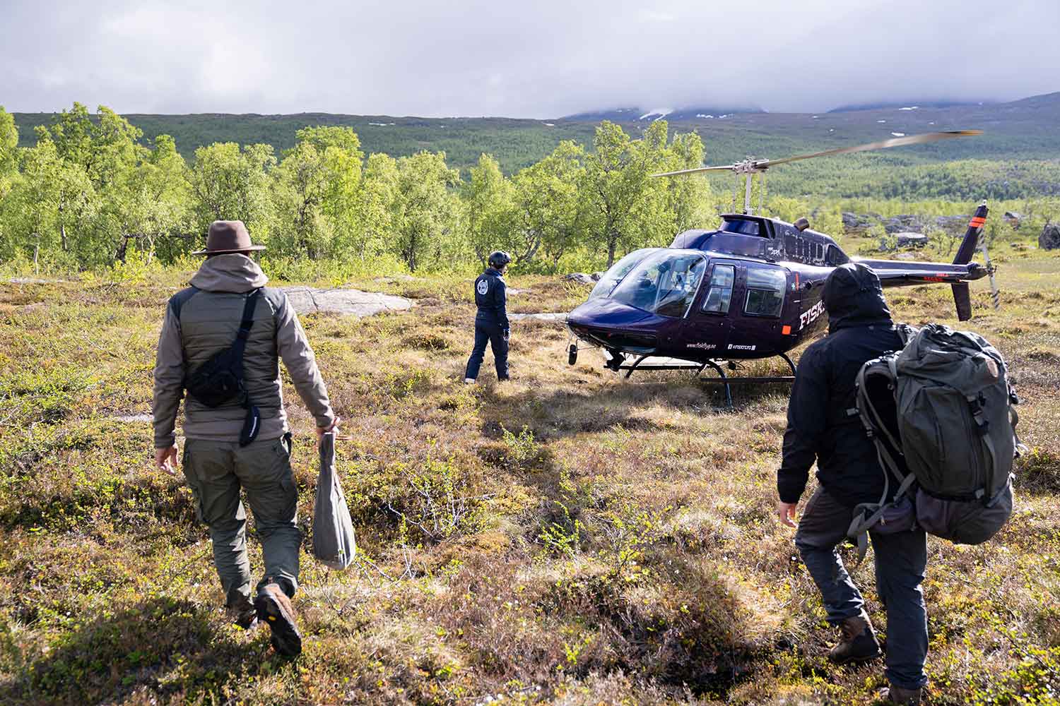 Teilnehmer unseres extrem Survival-Trainings laufen auf einen Hubschrauber in Schweden zu. Im Hintergrund sind Berge zu erkennen.