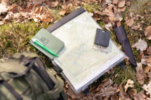 Eine Landkarte liegt mit einem Kompass und einem Notizblock auf dem Waldboden. In der Outdoor-Erste-Hilfe ist die Reisevorbereitung die besten Krisenintervention.