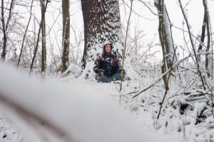 Ein Teilnehmer sitzt an einem Baum angelehnt im Schnee und meditiert. Durch eine Resilienz-Training und Mentales-Training kann die Wahrnehmung geschult, die sinne geschärft und die Psyche abgehärtet werden.