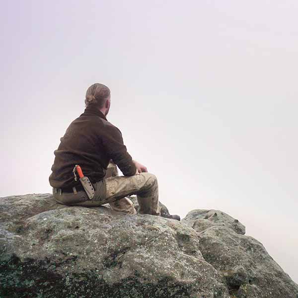 Ein Mann sitzt auf einem Felsen und schaut in die Weiter. Das Symbolbild steht für die Stärkung der Willenskraft, Resilienz und Wahrnehmung in unserem Survival-Psychologie Kurs.