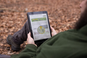 Ein Jagdschüler sitzt an einem Baum angelehnt auf dem Waldboden. Er lern mit dem Online-Lernsystem im Eigenstudium, bevor der zu uns in die Jagdschule kommt.