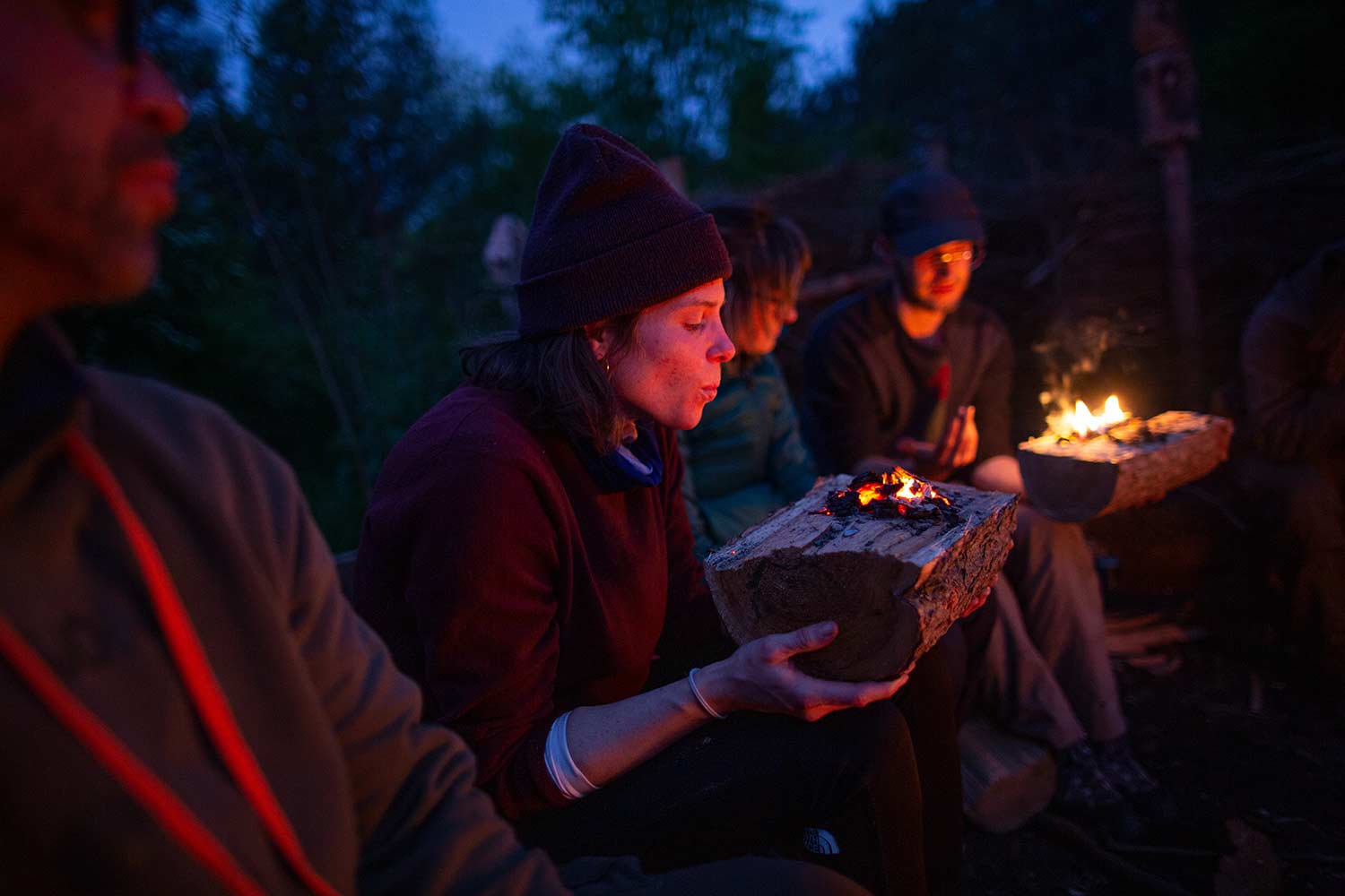 Eine Teilnehmerin sitzt mit der Gruppe am Lagerfeuer und brennt sich mit Glut eine Schüssel aus Holz. Dieses Handwerk gehört zu den Kernroutinen der Wildnispädagogik
